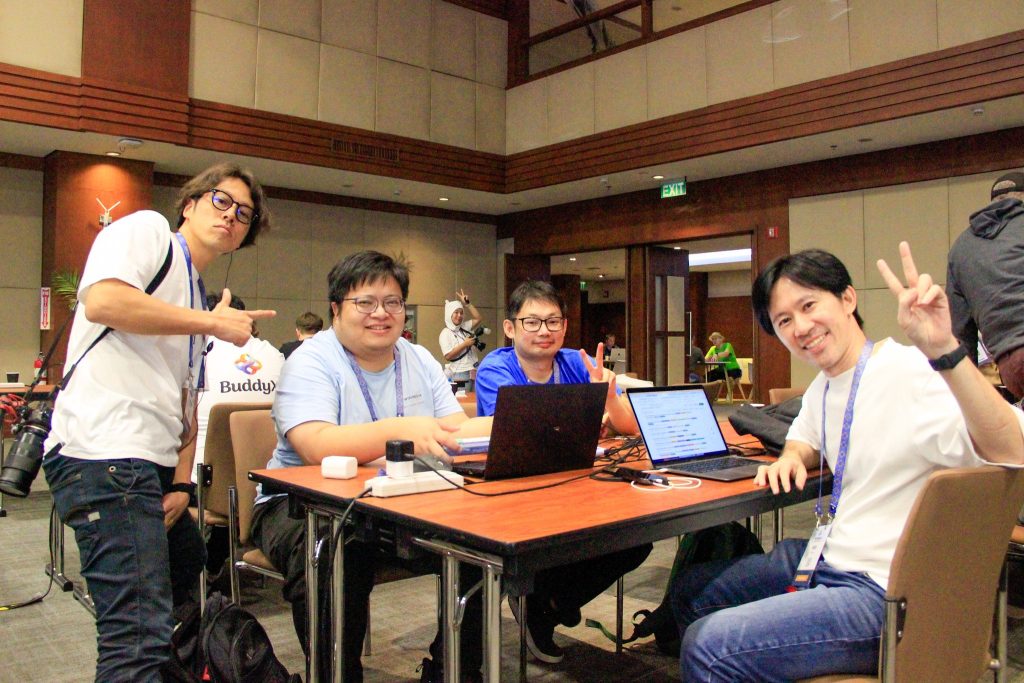 Four attendees sitting around a table with laptops, smiling and posing while working during Contributor Day.