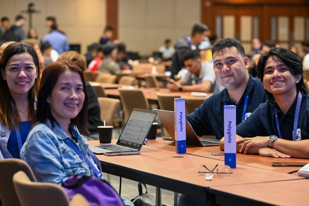 Four WordCamp Asia attendees sitting together at the Polyglots table, smiling while working on their laptops during Contributor Day.